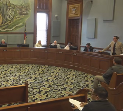 Ron Smith, City Manager for the City of Statesville, presents the April 2026 City Manager Update during a City Council meeting at City Hall. Standing at the podium inside the council chambers, Smith addresses the Mayor and Council members seated along the curved dais beneath the large City seal mural. Members of the public are also visible attending the meeting from the audience seating area.