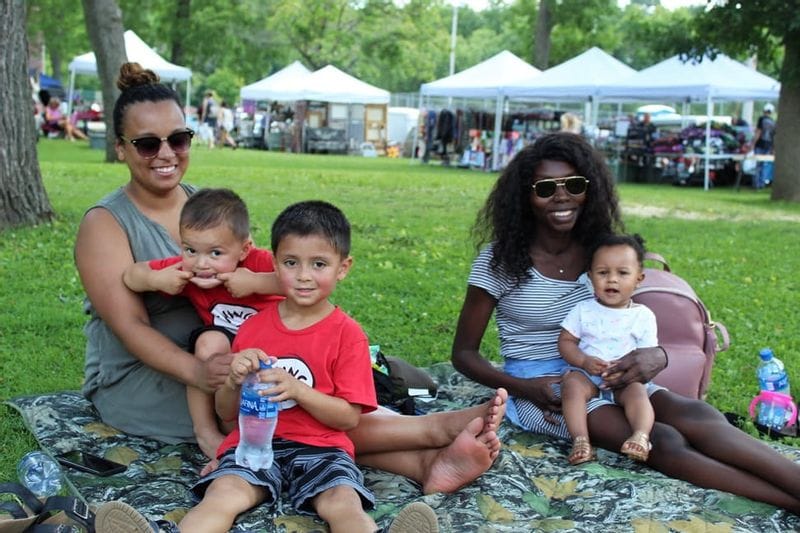Two women and three children smiling while sitting on blankets in Lanesboro's Sylvan Park during Buffalo Bill Days