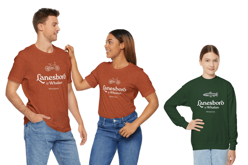 Three models wearing Lanesboro & Whalan, Minnesota apparel: two adults in rust-colored T-shirts with a bicycle graphic and one person in a green sweatshirt with a fish graphic.