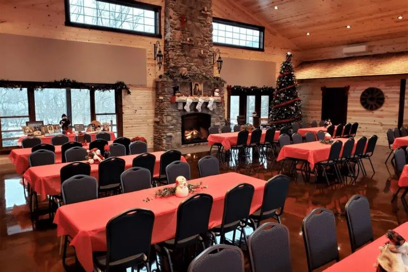 A festively decorated dining and gathering space at the Cedar Valley Retreat Center features long tables with red tablecloths, a large stone fireplace with holiday décor, and a Christmas tree, creating a warm, rustic atmosphere for seasonal events.