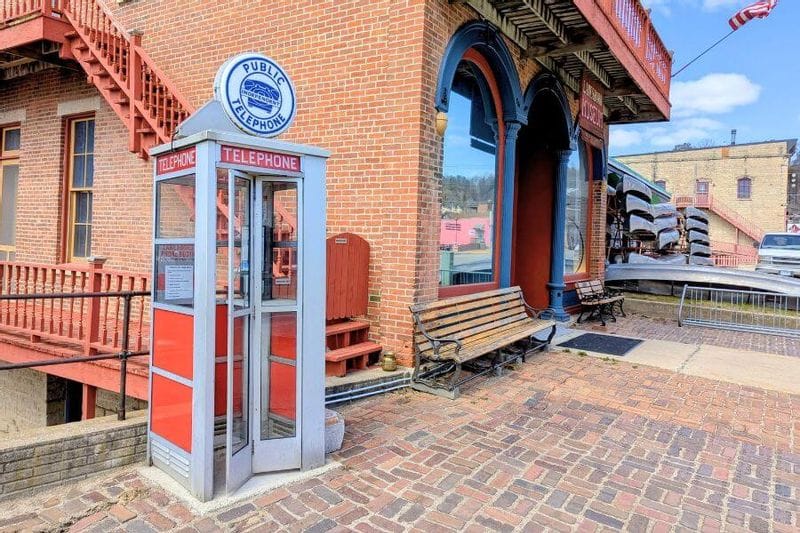 Historic public telephone booth outside the Lanesboro Museum, set along a brick walkway beside the museum’s red brick building and arched windows in downtown Lanesboro.