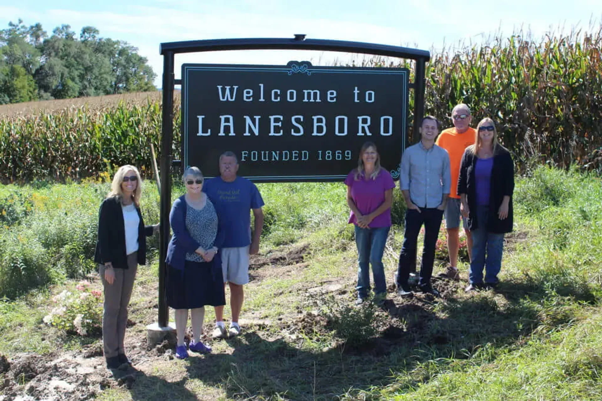 Community members stand beside the Welcome to Lanesboro sign at the entrance to Lanesboro, Minnesota.