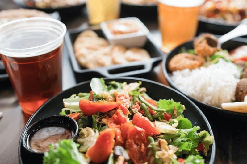 A fresh salad topped with vegetables sits on a table alongside craft beer, bread, and plated meals, highlighting a casual dining experience in Lanesboro.