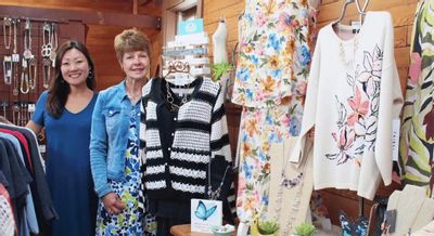 Two women stand inside a Lanesboro boutique surrounded by colorful dresses, sweaters, jewelry, and accessories, highlighting local shopping and small-town style.