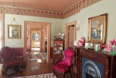 An elegant interior room at the Thompson House features Victorian-era décor, ornate wallpaper borders, antique furniture, and a decorative fireplace, offering a glimpse into historic lodging in Lanesboro, Minnesota.