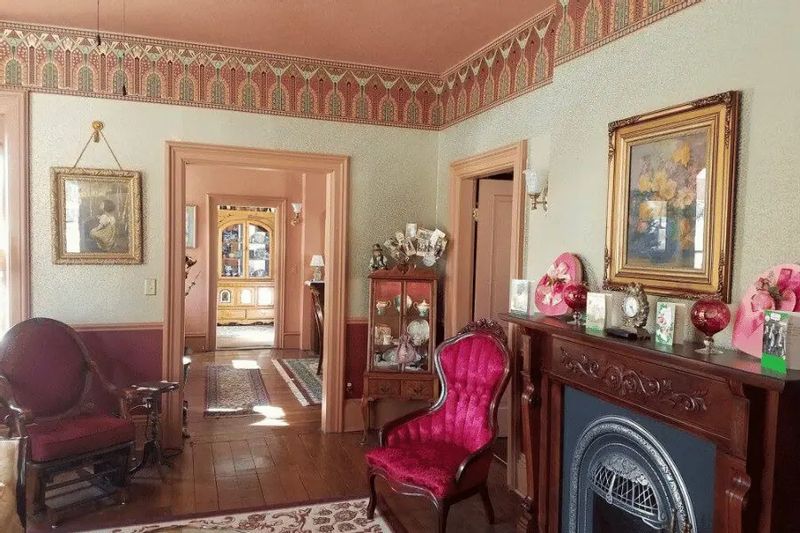 An elegant interior room at the Thompson House features Victorian-era décor, ornate wallpaper borders, antique furniture, and a decorative fireplace, offering a glimpse into historic lodging in Lanesboro, Minnesota.