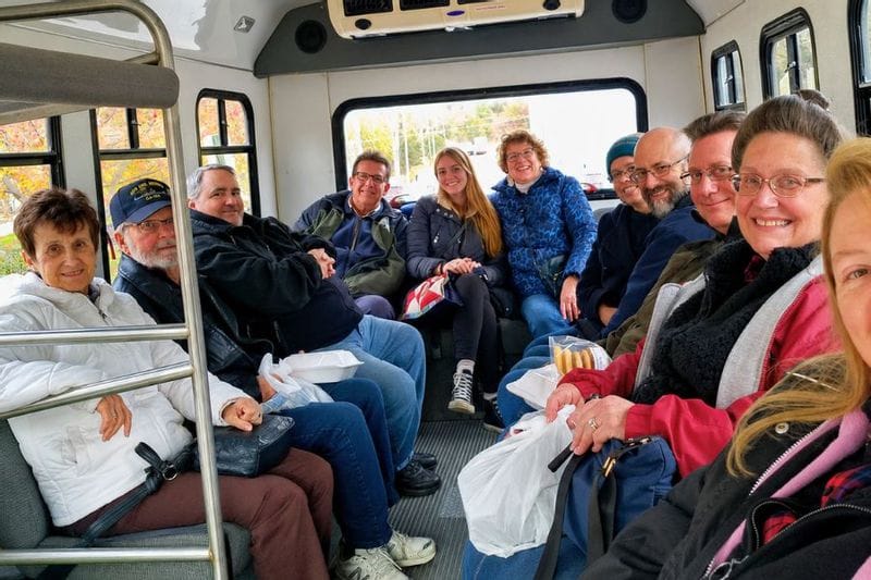 A group of people on an Amish tour bus smiling, with some holding bags and baked goods from local Amish shops