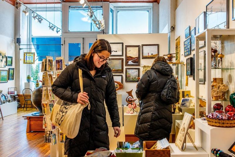 Visitors browse jewelry and artwork inside Lanesboro Arts Gallery, with local art displays and a portrait painting visible in the background.