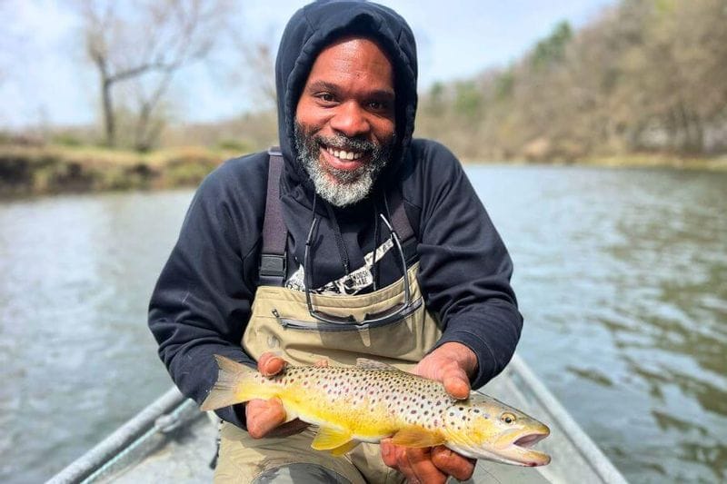 Smiling angler holding a freshly caught brown trout while fishing on the Root River in Lanesboro, Minnesota.