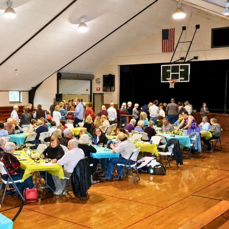 A group of people gathered for a banquet, with tables and chairs set up in the gym at the Lanesboro Community Center