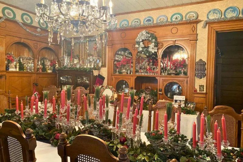 A festively decorated dining room at Oakenwald Terrace during a Christmas open house, featuring a long table set with red candles, greenery, crystal glassware, and historic wood furnishings.