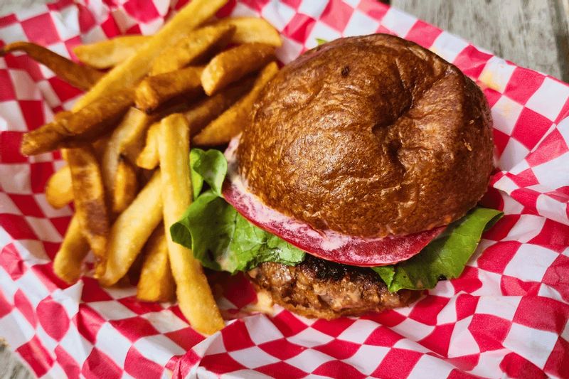 A freshly made burger with lettuce on a toasted bun is served alongside golden fries in a red-and-white checkered basket, highlighting a classic meal from a local eatery.