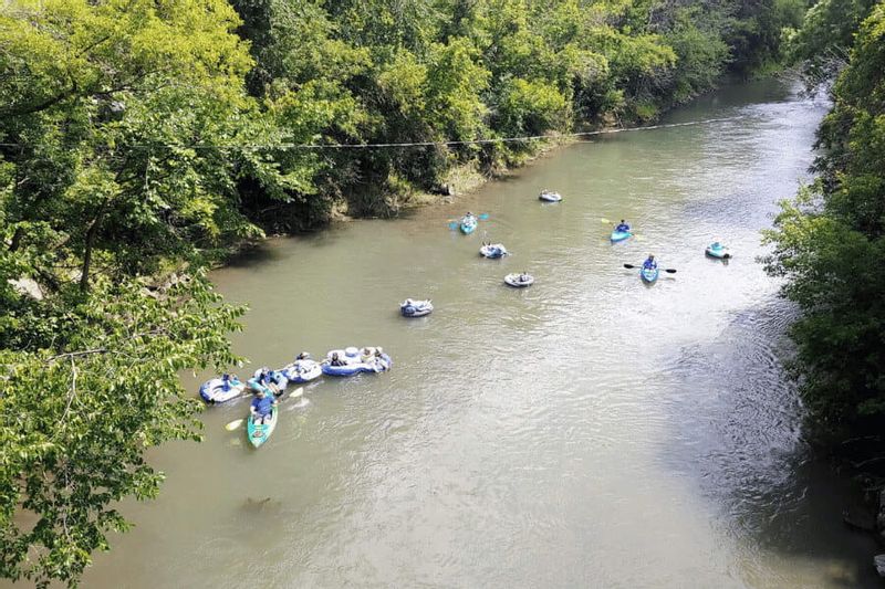 Kayakers and tubers float down the Root River through a tree-lined stretch near Lanesboro, enjoying a sunny day of summer recreation in southeastern Minnesota.