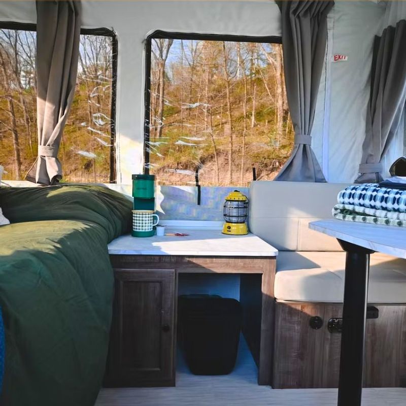 Interior of a camper rental in Lanesboro, Minnesota, showing a cozy sleeping and seating area with windows overlooking wooded Bluff Country scenery