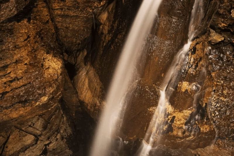 Water cascades down a rocky cave wall inside Niagara Cave, highlighting textured stone surfaces and flowing water illuminated in warm tones.