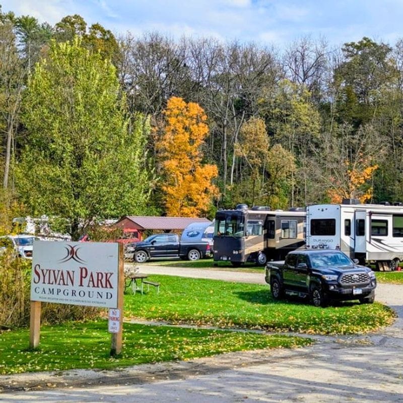 RVs and vehicles parked at Sylvan Park Campground in Lanesboro, Minnesota, surrounded by fall foliage and trees in autumn color.