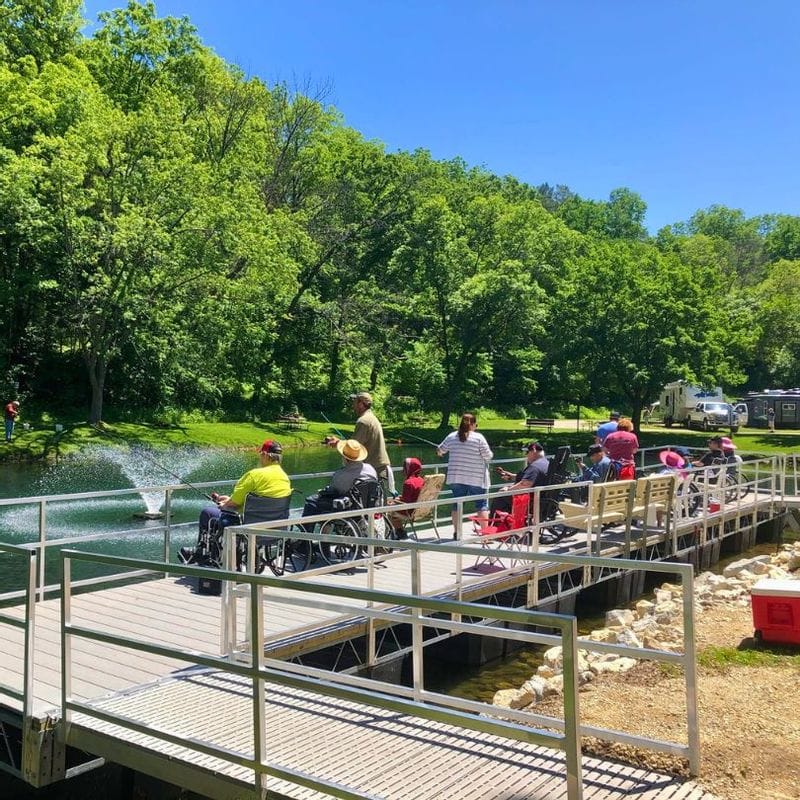 People fishing at a dock at a pond in Lanesboro's Sylvan Park on a sunny day surrounded by lush greenery