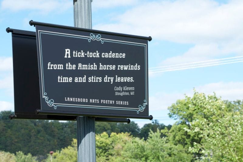 Poetry sign from the Lanesboro Arts Poetry Series displayed in the Poetry Parking Lot in Lanesboro, Minnesota, featuring a poem about Amish horses against a Bluff Country landscape backdrop