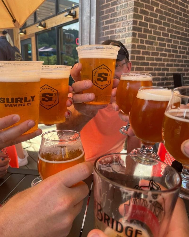 Several people's hands holding plastic cups of Surly beer and holding them up