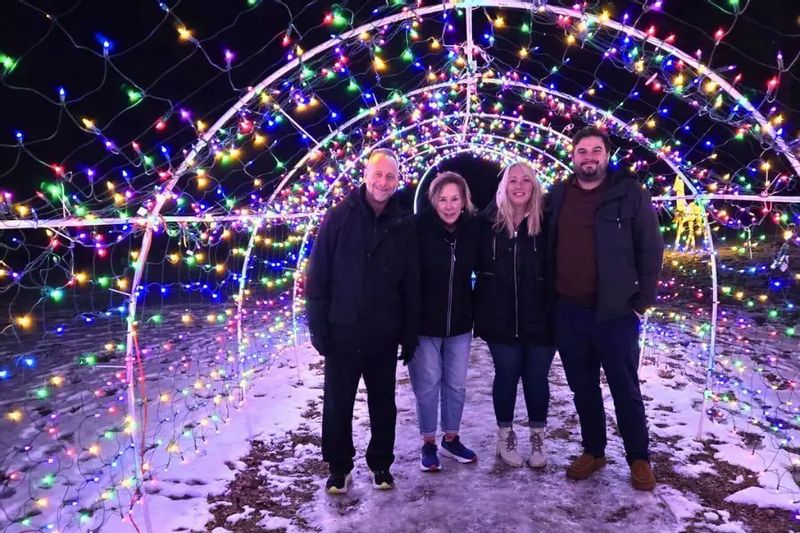 Four people stand together inside a glowing tunnel of colorful holiday lights at night, with snow on the ground during Lanesboro’s winter Legion Lights display.