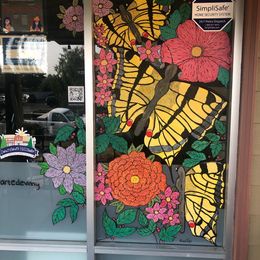 A temporary art installation at Massage Collective during the Spring Window takeover. Giant yellow and black Swallowtail butterflies surrounded by flower blossoms and leaves are painted on the window.  