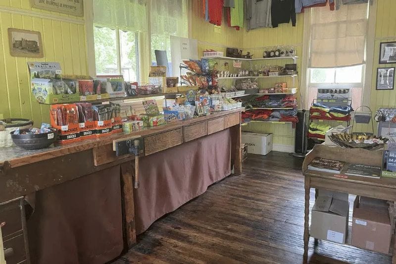 Shelves and counters inside the Whalan Depot display snacks, local food items, apparel, and gifts in a bright, welcoming shop with wood floors and yellow walls.