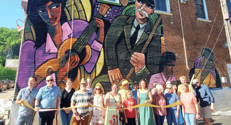 Community members gather for a ribbon-cutting in front of a large, colorful mural in Lanesborog.