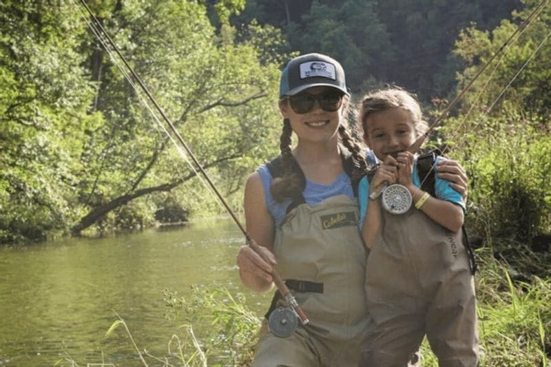 A mother and daughter holding fishing rods while fly fishing on a calm, tree-lined river near Lanesboro, Minnesota