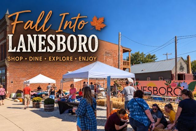 Visitors gather at an outdoor fall market in downtown Lanesboro, Minnesota, beneath a “Fall Into Lanesboro” banner inviting people to shop, dine, explore, and enjoy.