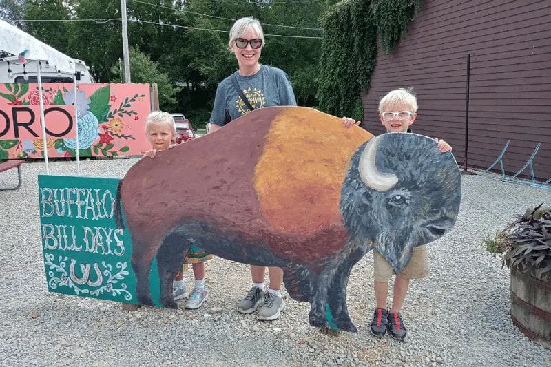 A mother and two children pose behind a painted buffalo cutout during Buffalo Bill Days in Lanesboro, smiling at a family-friendly summer festival display.