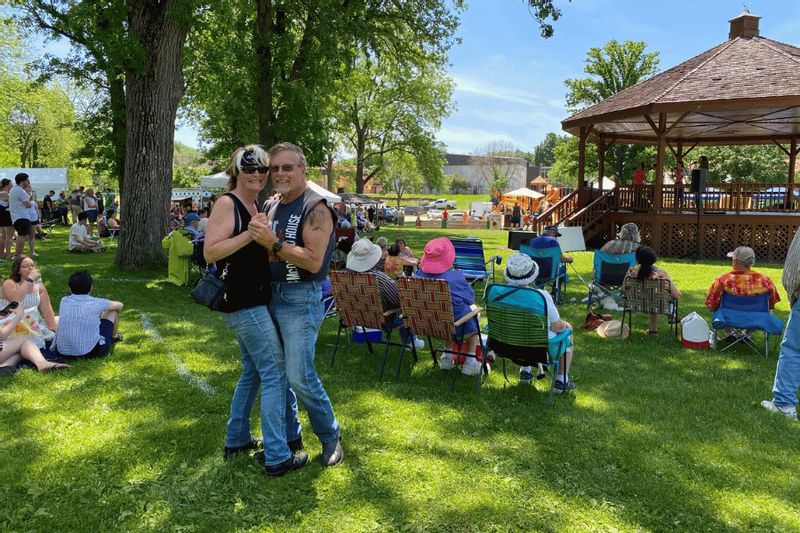 A couple dances together on the grass in Lanesboro as a crowd relaxes in lawn chairs near a gazebo during a lively outdoor community event.
