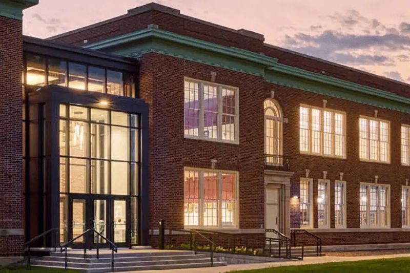 The Chatfield Center for the Arts exterior at dusk, showing the historic brick building with large illuminated windows and a modern glass entrance.