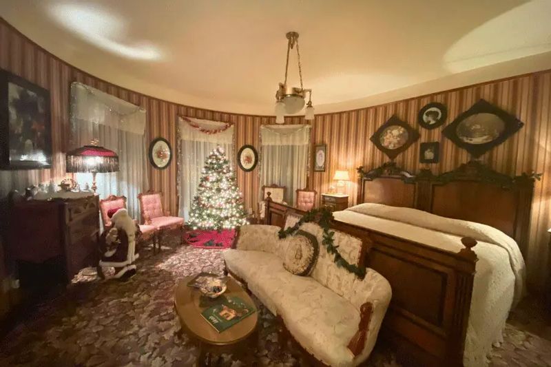 A festively decorated guest room at Oakenwald Terrace in Chatfield during the holidays, featuring a Christmas tree, vintage furnishings, garlands, and warm lighting in a historic Victorian setting.