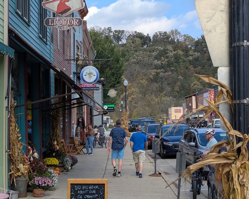 People stroll along downtown Lanesboro, Minnesota, with shops, fall decorations, and bluffs in the background.