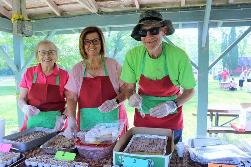 Volunteers in red and green aprons serve rhubarb treats during the Lanesboro Rhubarb Festival tasting contest in Sylvan Park.