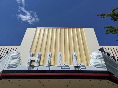 A view looking up past the newly built yellow façade and white neon letters spelling out "HILL" with a blue sky containing one wispy cloud above. 