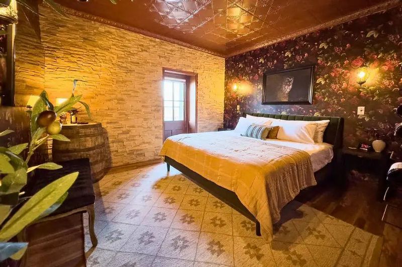 The Merlot Room at Hotel Lanesboro, featuring a king bed, patterned tile floor, floral accent wall, and warm lighting that creates a cozy, upscale atmosphere.
