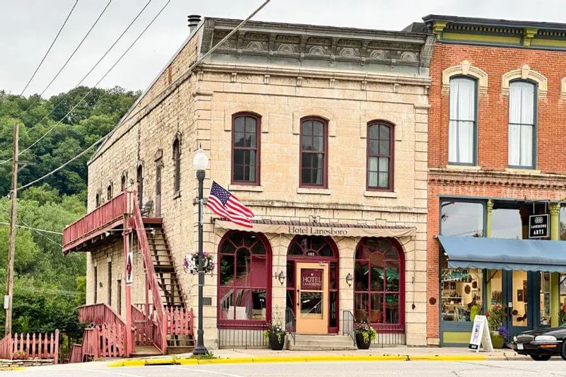 The historic Hotel Lanesboro building in downtown Lanesboro, with its stone façade, arched windows, exterior staircase, and an American flag flying along the street.