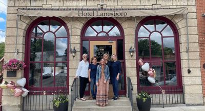 Staff members stand on the front steps of Hotel Lanesboro beneath the building’s historic stone façade and arched windows, marking a special occasion at the downtown hotel.