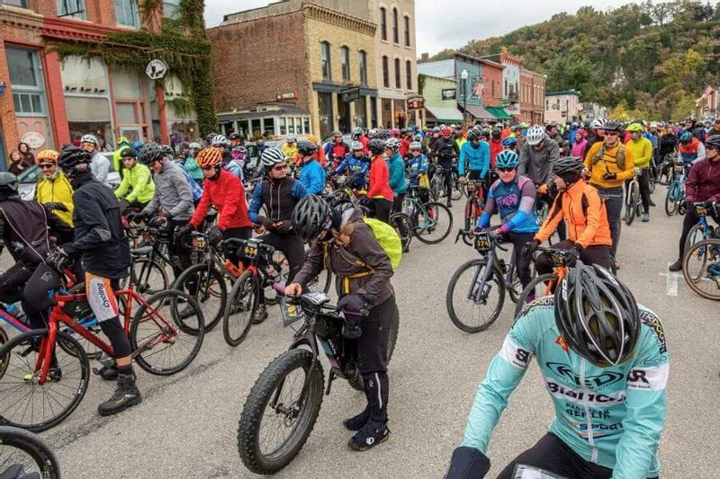 Hundreds of cyclists line up at the starting line of the Filthy 50 gravel race on downtown Lanesboro’s main street, surrounded by historic storefronts and fall hillsides.