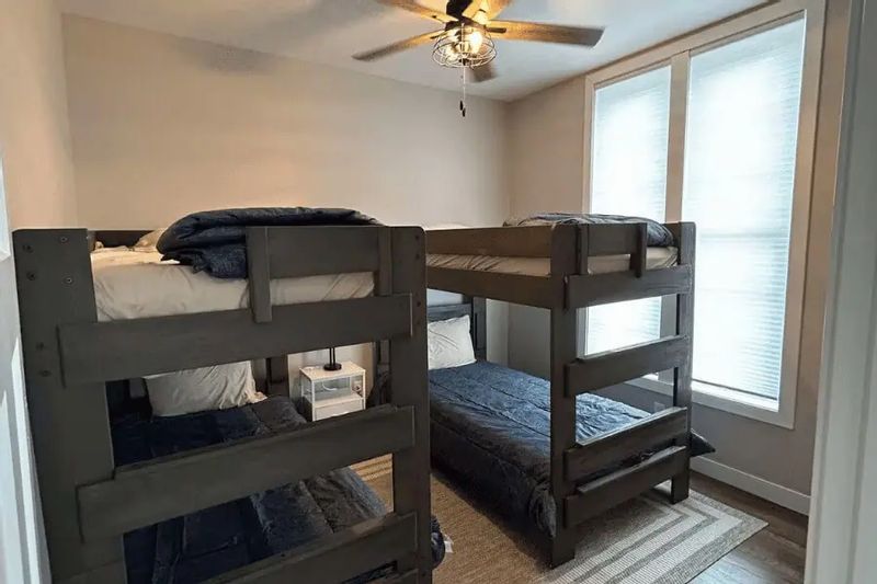 A bedroom at Parkway Place features sturdy bunk beds with blue bedding, a ceiling fan, and large windows that bring in natural light, making it a comfortable space for families or groups staying in downtown Lanesboro.