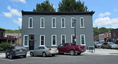 Parkway Place is shown as a restored gray historic building with tall windows along Main Street in downtown Lanesboro, with parked cars and neighboring storefronts visible on a sunny day.
