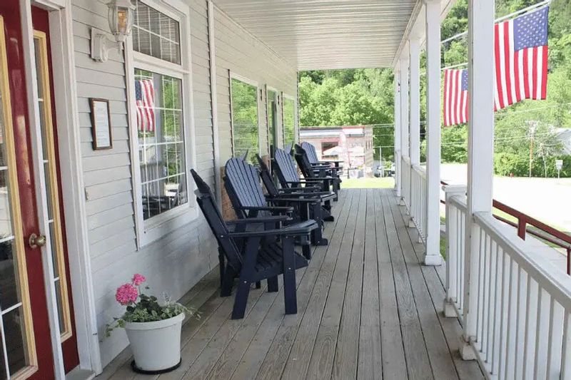 The front porch at the Cottage House Inn features a row of black rocking chairs, white railings, and American flags, offering a relaxed place for guests to sit and enjoy views of downtown Lanesboro.