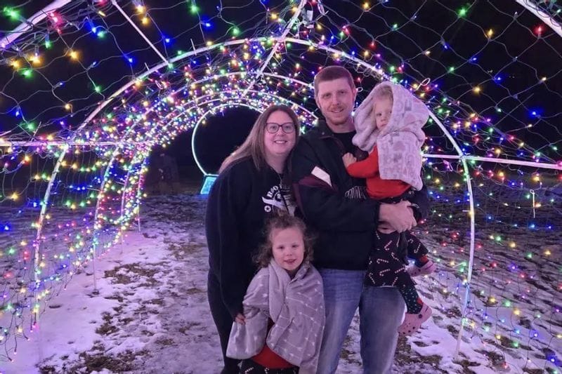 A family poses together beneath a tunnel of colorful holiday lights at Legion Lights in Lanesboro during a winter evening.