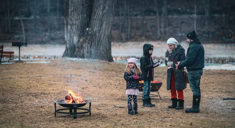 Family enjoying a winter evening bonfire with s’mores during Lanesboro Legion Lights, gathered around a fire pit in a snowy park